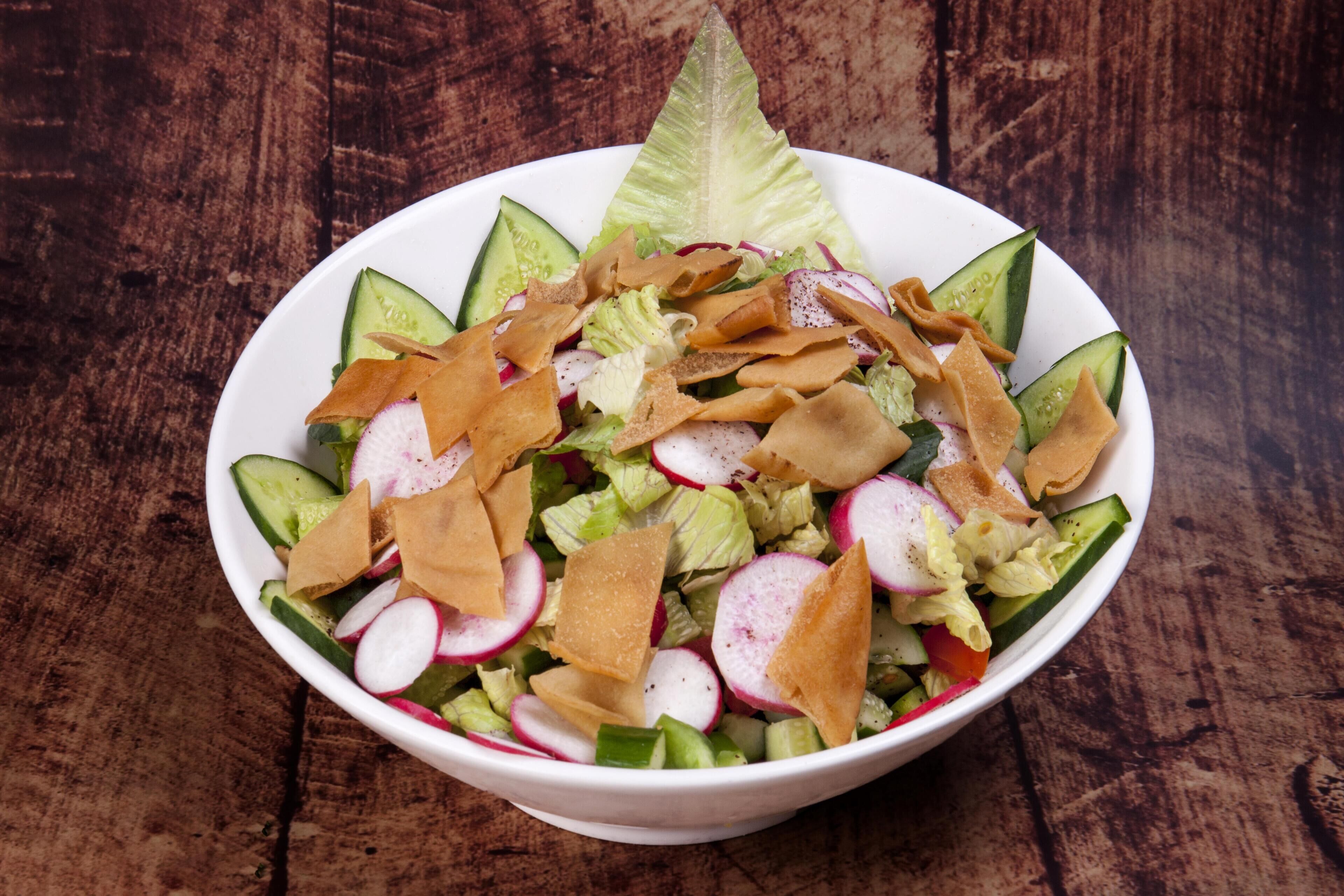 Un tazón de ensalada con lechuga, pepinos, rábanos y chips de pita sobre una mesa de madera.