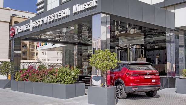 Un edificio moderno con entrada de vidrio y un coche rojo estacionado en la parte delantera.