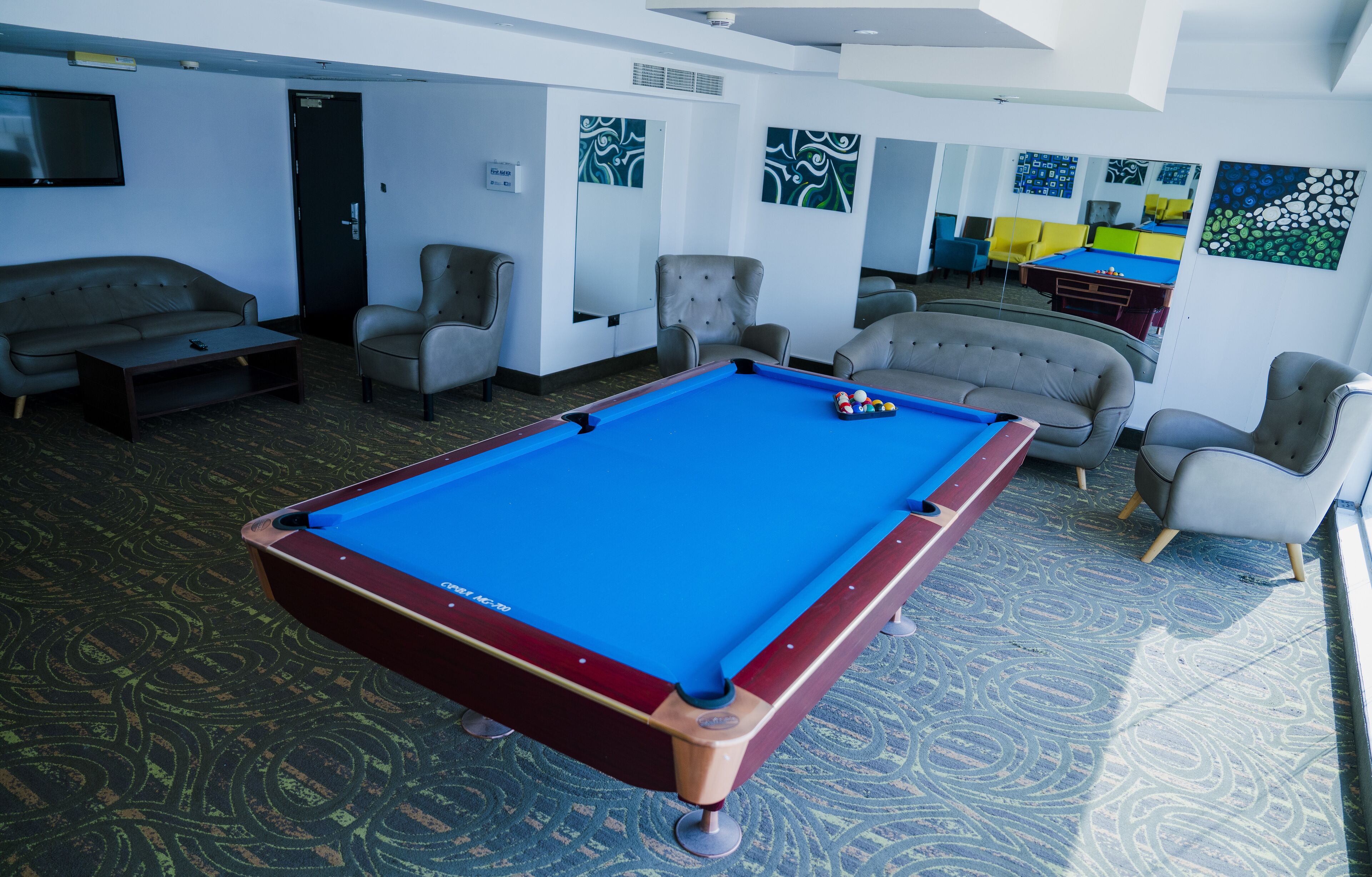 A pool table in a room with a patterned carpet, several armchairs, and a sofa.