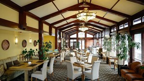 A spacious indoor area with high ceilings, wooden beams, and large windows allowing natural light. Tables and chairs are arranged for dining or meetings. - Samal Resort & Spa (Almaty)