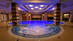 A large indoor swimming pool with a central hot tub, surrounded by seating areas and a reception desk. - Samal Resort & Spa (Almaty)