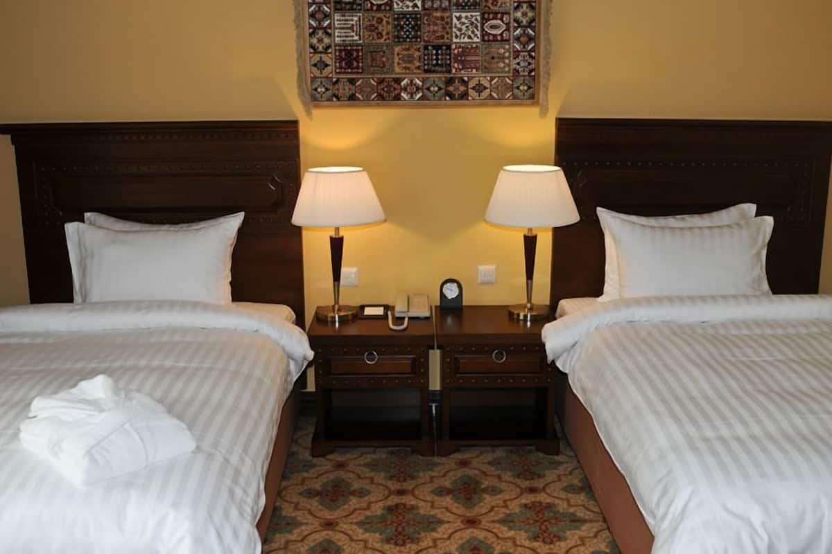 A hotel room with two beds, a nightstand with lamps, a clock, and a decorative tile wall.