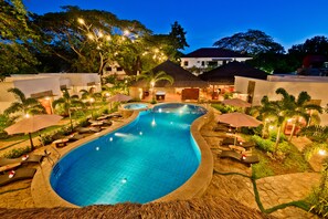 A swimming pool with lounge chairs and umbrellas, surrounded by greenery and buildings. - Acacia Tree Garden Hotel (Puerto Princesa)