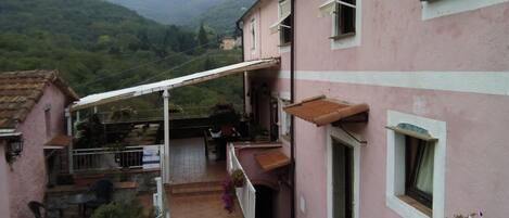 A pink building with a balcony, outdoor seating, and a view of green hills.