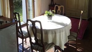 Een eethoek met een ronde tafel, stoelen, een potplant en uitzicht op het buiten.
