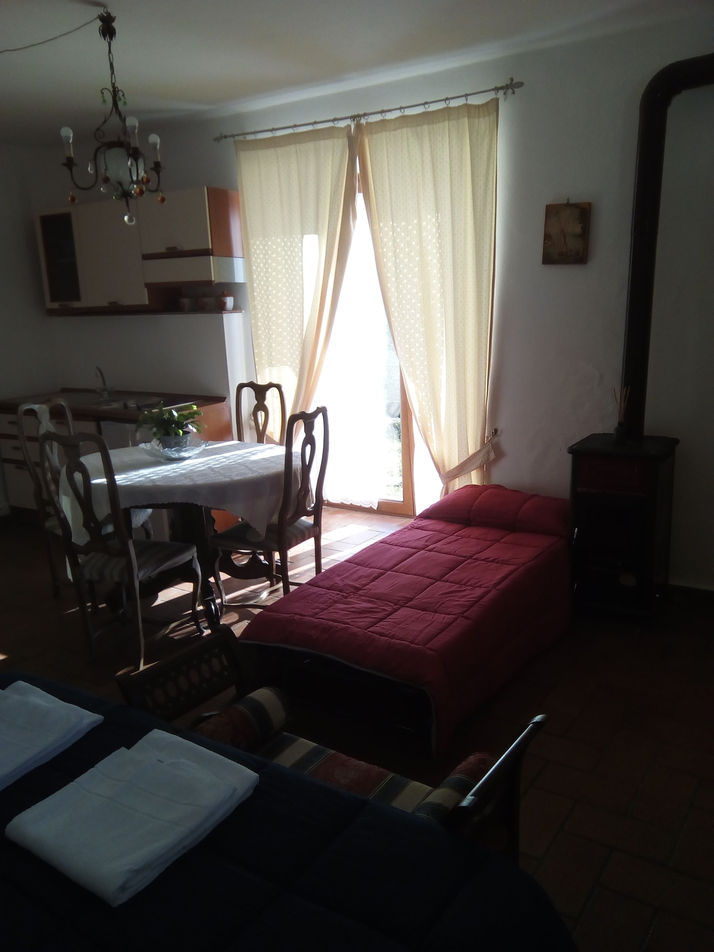 A room with a bed, a dining table with chairs, a chandelier, and a window with curtains.