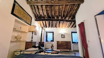 Un dormitorio con techo de madera, cama, mesita de noche con lámpara, cómoda y ventana con cortinas.