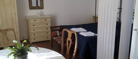 Una habitación con una mesa redonda, sillas, un aparador, una cama con dosel y una ventana.