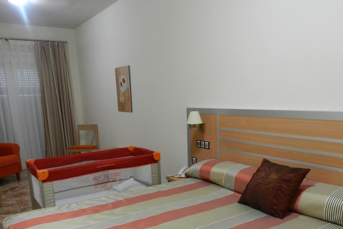 A hotel room with a bed, a small table, a chair, a lamp, and a painting on the wall.