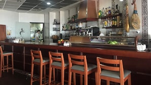 Zona bar con sedie di legno, un bancone con bottiglie e una cucina sullo sfondo.
