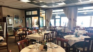 Una sala ristorante con tavoli rotondi apparecchiati, con tovaglie bianche e posate ordinate.