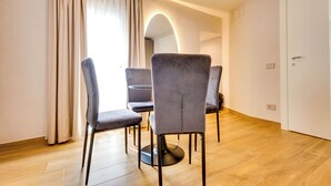 A modern dining area with a round table and four grey chairs, a wooden floor, and a white door in the background. - Relais Badoer (Rome)