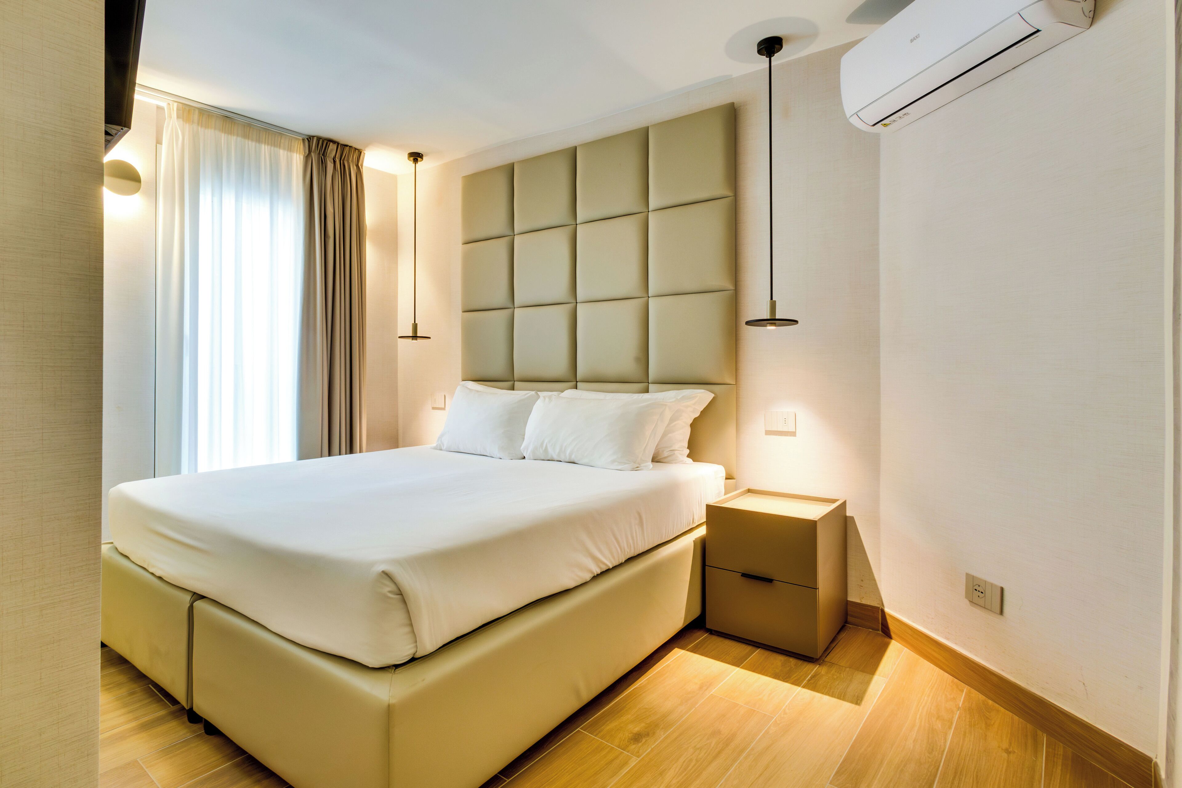 Ein modernes Hotelzimmer mit einem großen Bett, Nachttischen, einer Klimaanlage und einem Fenster mit Vorhängen.