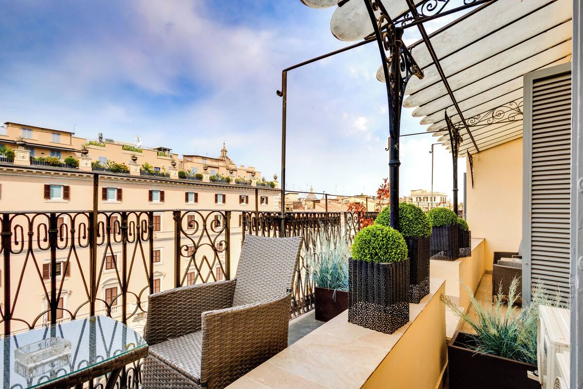 A balcony with wicker furniture, potted plants, and a view of buildings in the background.