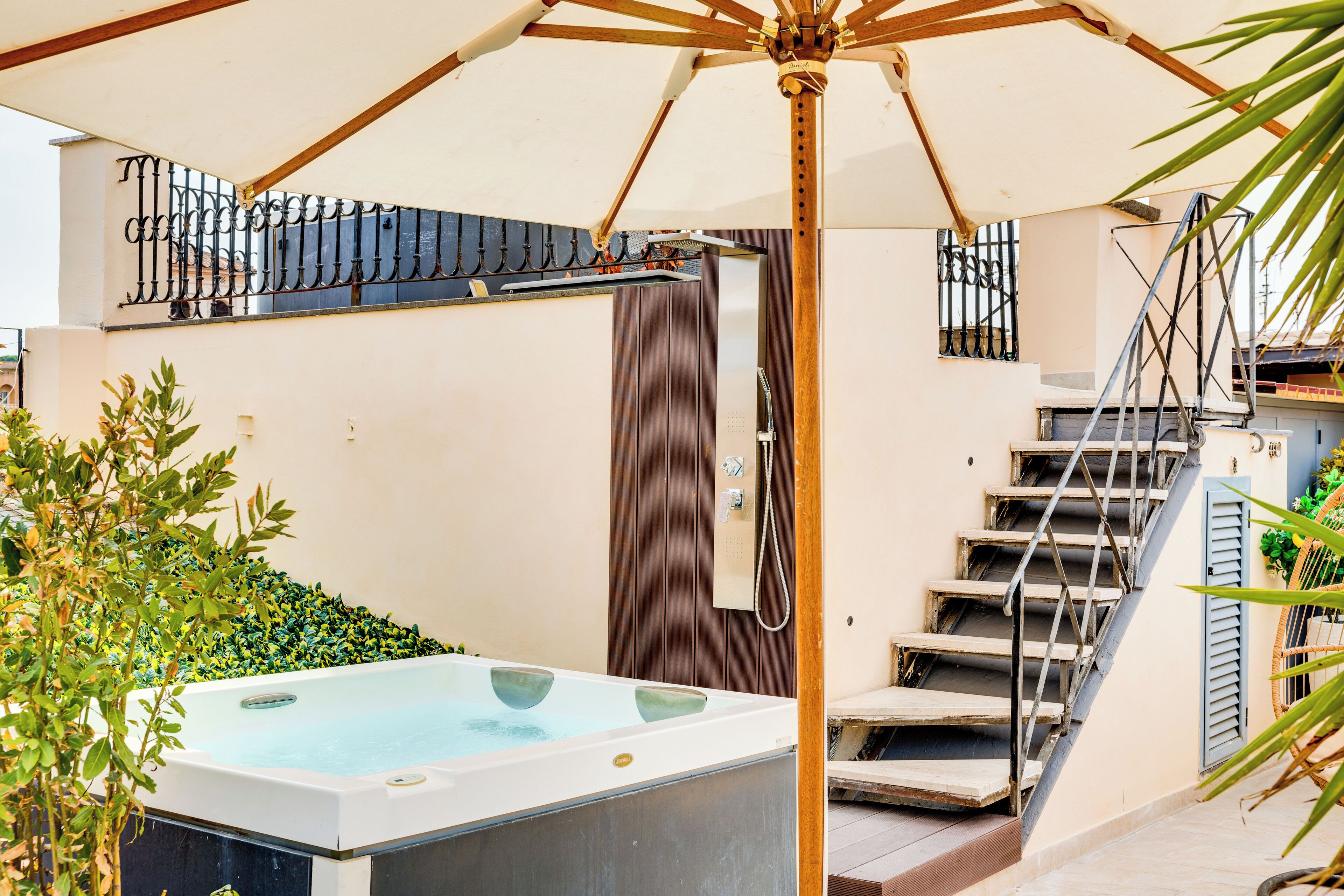 A hot tub under an umbrella, a wooden staircase, and a metal railing.