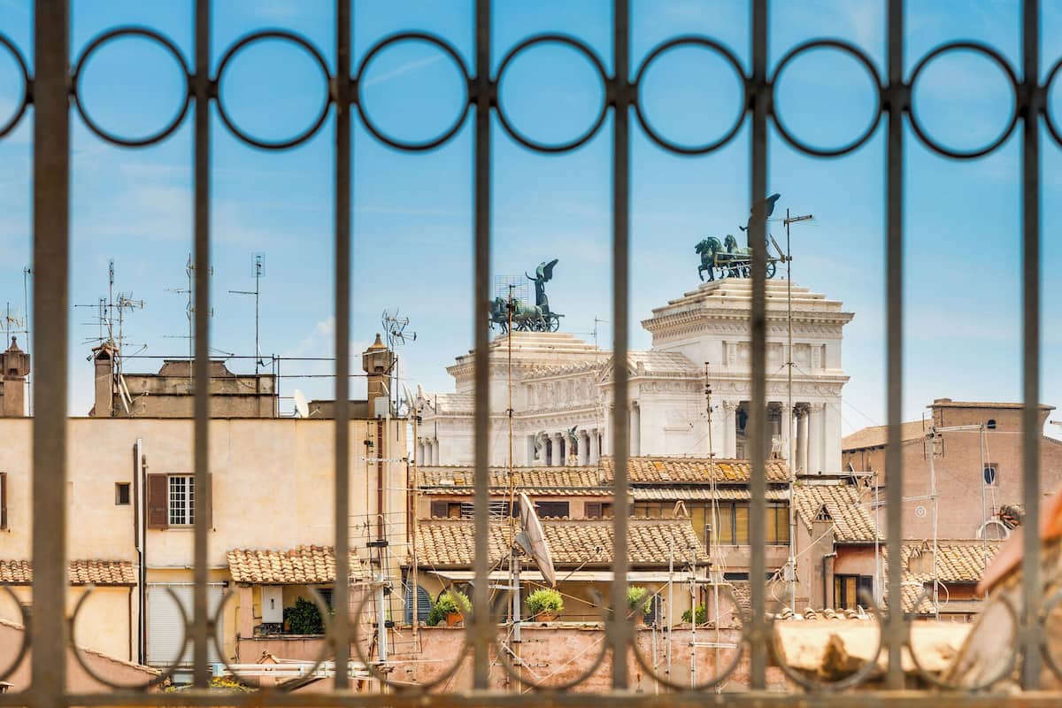 A view of a historic building with classical architecture, including columns and statues, through a metal fence.