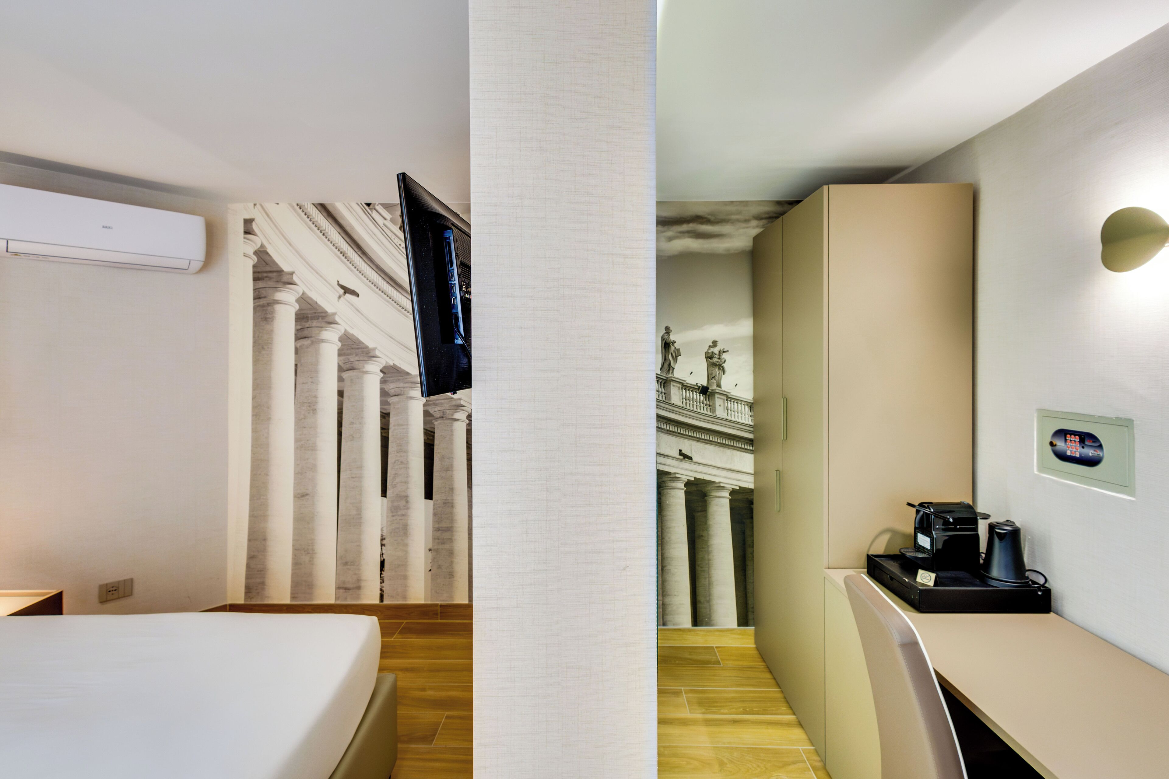 Habitación de hotel con una cama, televisión de pantalla plana, cafetera y vista a una escalera monumental.