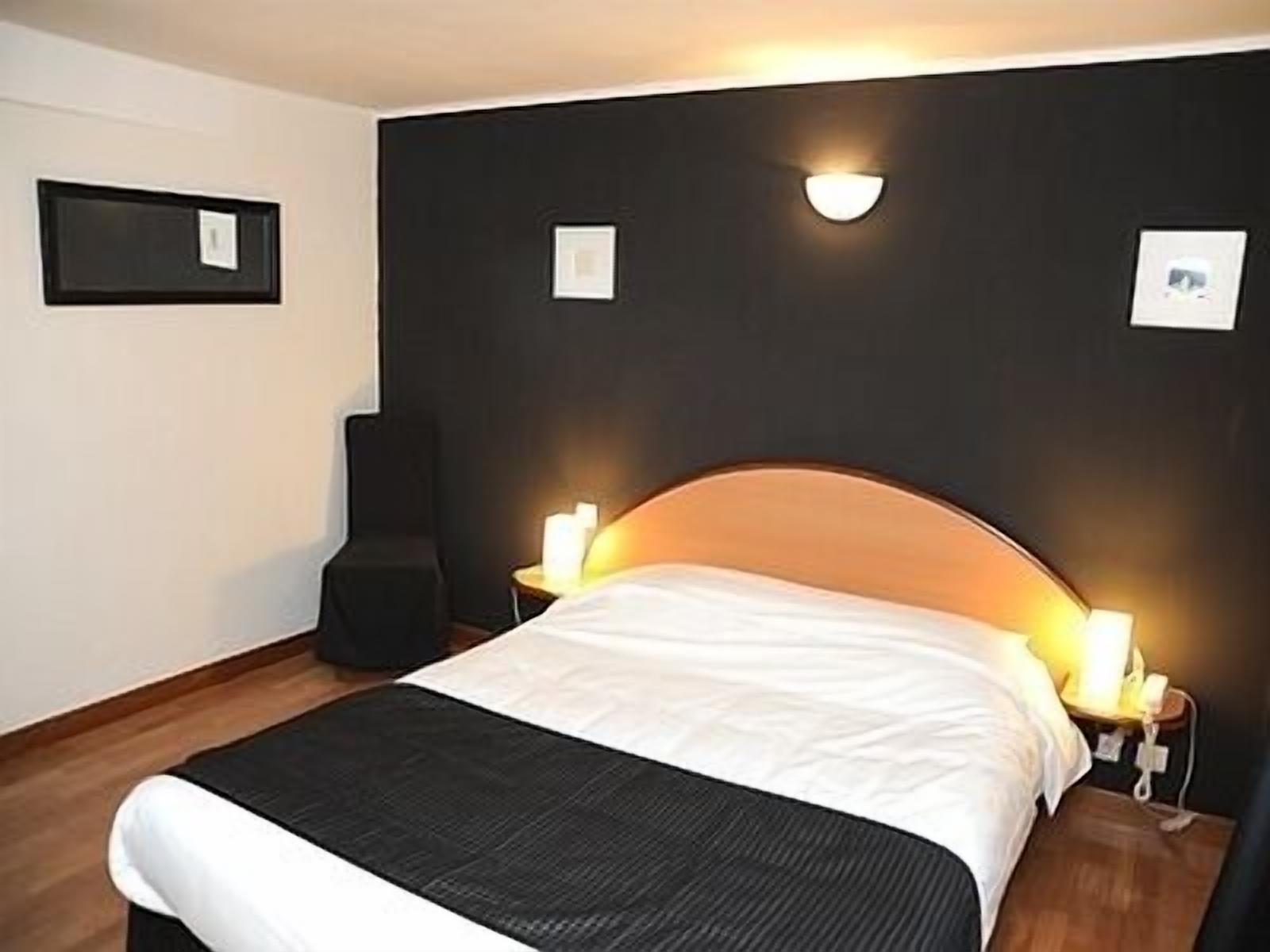 Ein modernes Hotelzimmer mit einem großen Bett, zwei Nachttischlampen, einem schwarzen Kopfteil und gerahmten Bildern an der Wand.
