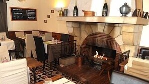 A restaurant with a stone fireplace, tables with white tablecloths, and a menu board on the wall. - Hôtel de l'Ecu de France (Le Malesherbois)