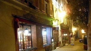 A narrow street with buildings on either side, featuring storefronts with illuminated signs and windows. - Hôtel de l'Ecu de France (Le Malesherbois)