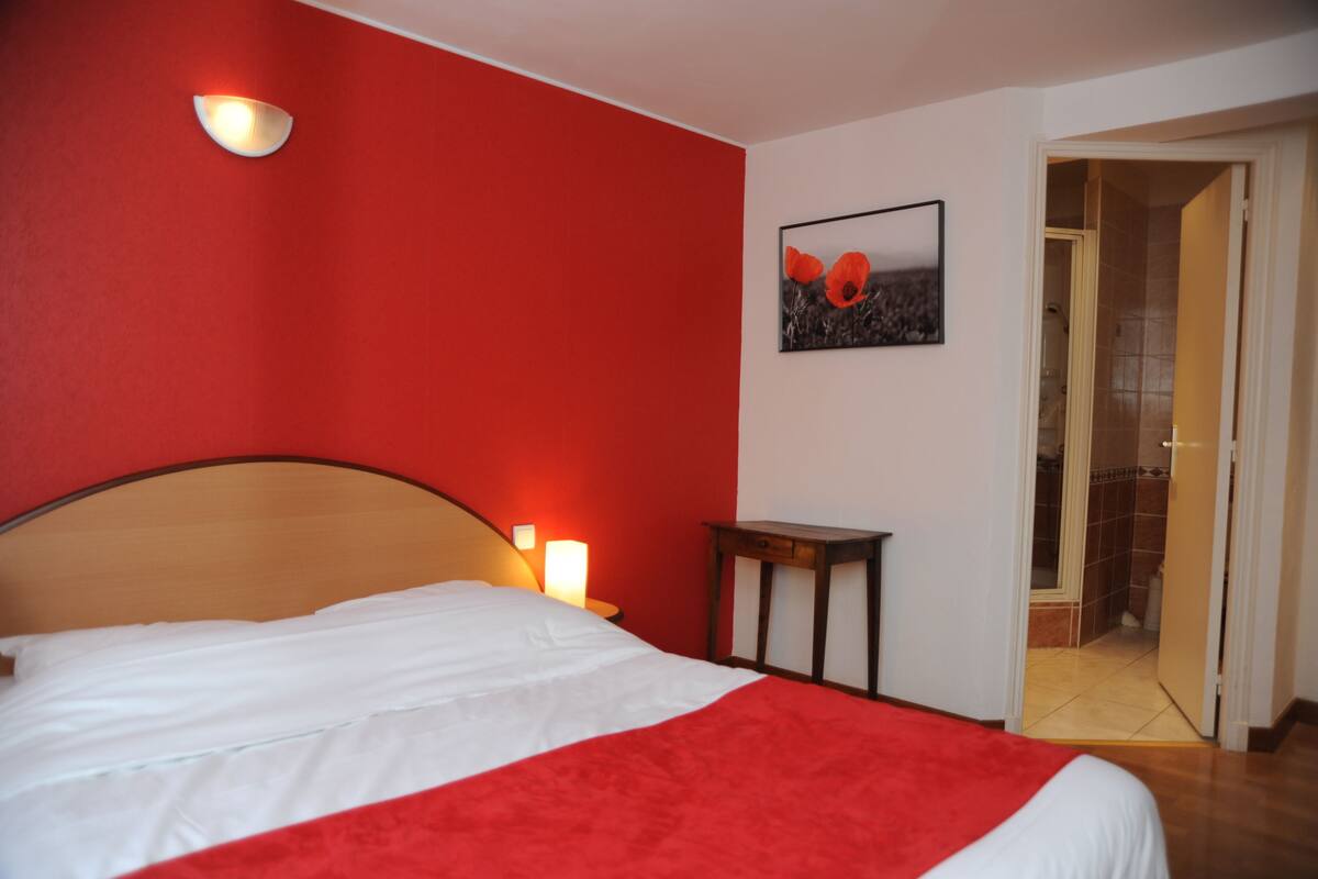 A hotel room with a bed, a wall-mounted light, a small table, and a door leading to a bathroom.