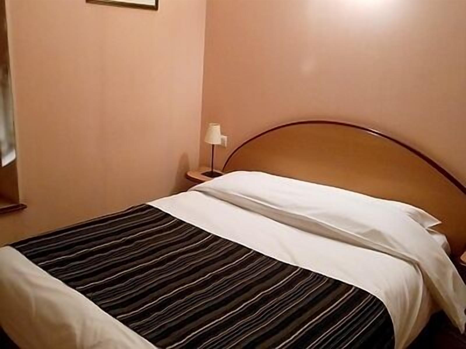 Quarto de hotel com cama, mesa de cabeceira e abajur.