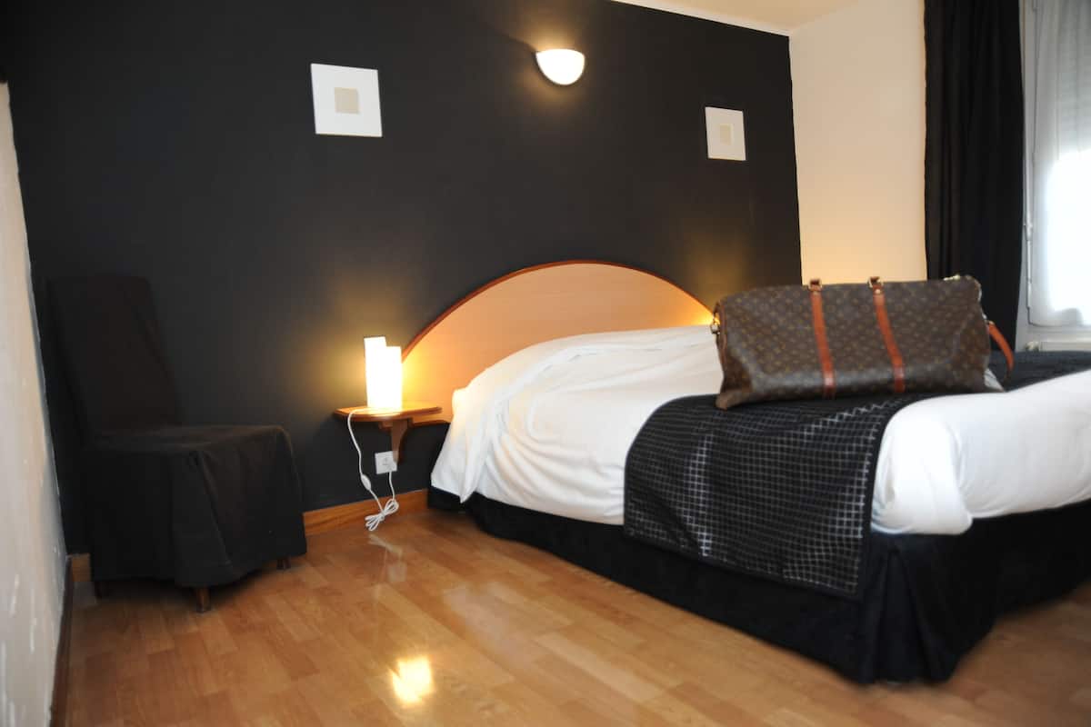 A hotel room with a bed, a chair, a nightstand, and a lamp.