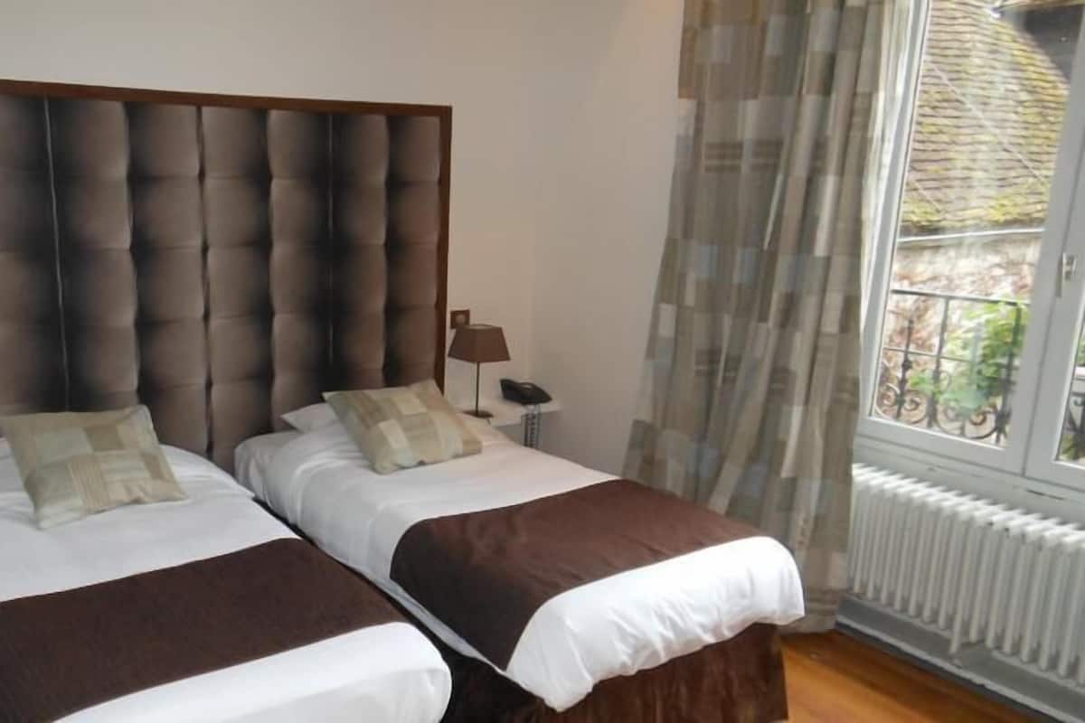 A double bed with a tufted headboard, two bedside tables with lamps, and a window with a view of greenery.