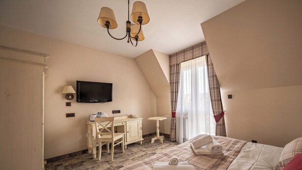 Habitación de hotel con cama, escritorio, televisor y ventana con cortinas.