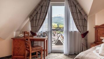 Un dormitorio con cama, un escritorio de madera con silla, teléfono y vistas a montañas a través de una ventana.