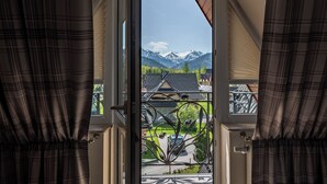 Vista a través de una puerta con reja metálica que da a un balcón, con vistas a un paisaje montañoso.
