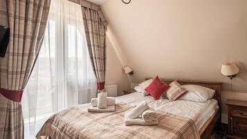 Habitación de hotel con cama, dos lámparas de noche, ventana con cortinas y radiador.