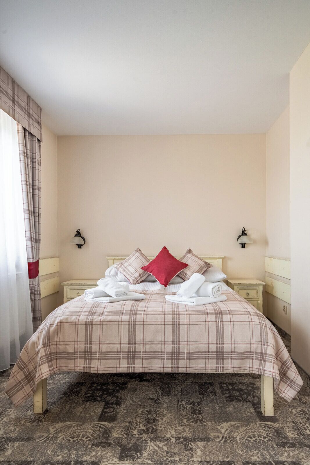 Habitación de hotel con cama, mesita de noche, lámpara y ventana con cortinas.