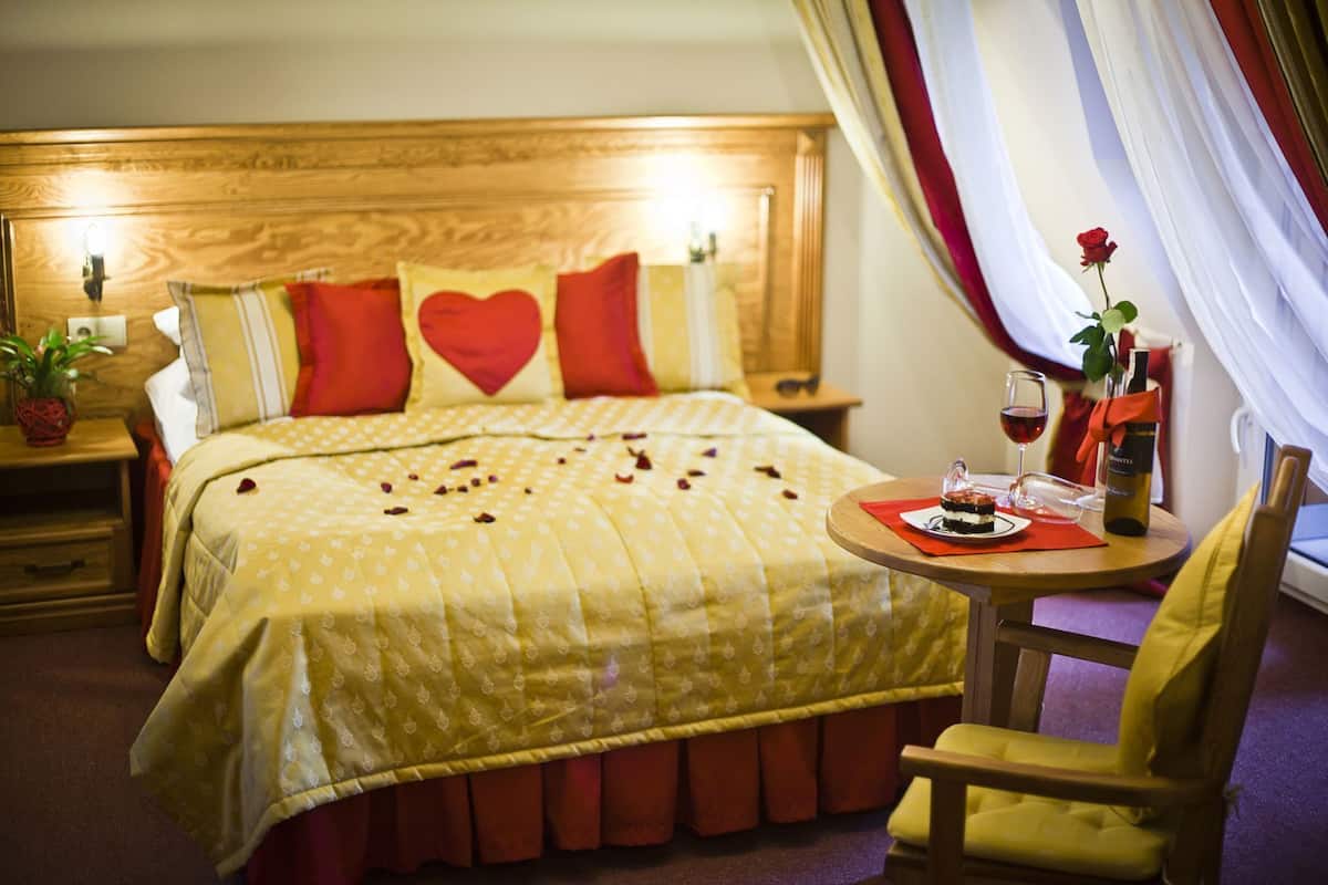 A hotel room with a bed, a bedside table with a bottle of wine, a glass, and a rose.