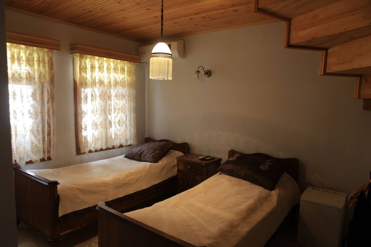 Une chambre avec deux lits en bois, une table de chevet, une lampe fixée au mur et un radiateur.