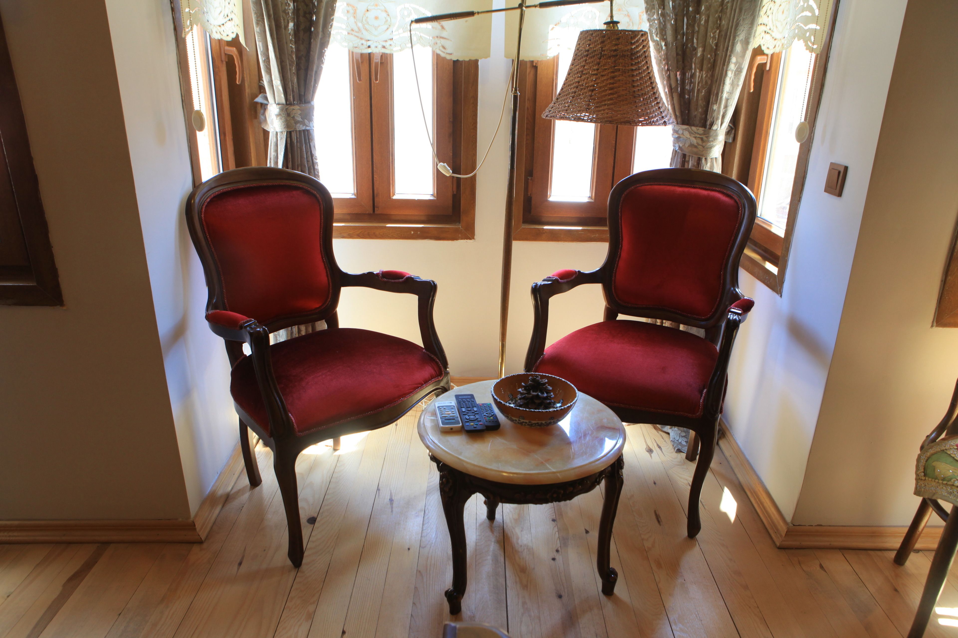 Two red upholstered chairs with wooden legs, a small round table with a bowl and remote controls, and a floor lamp.