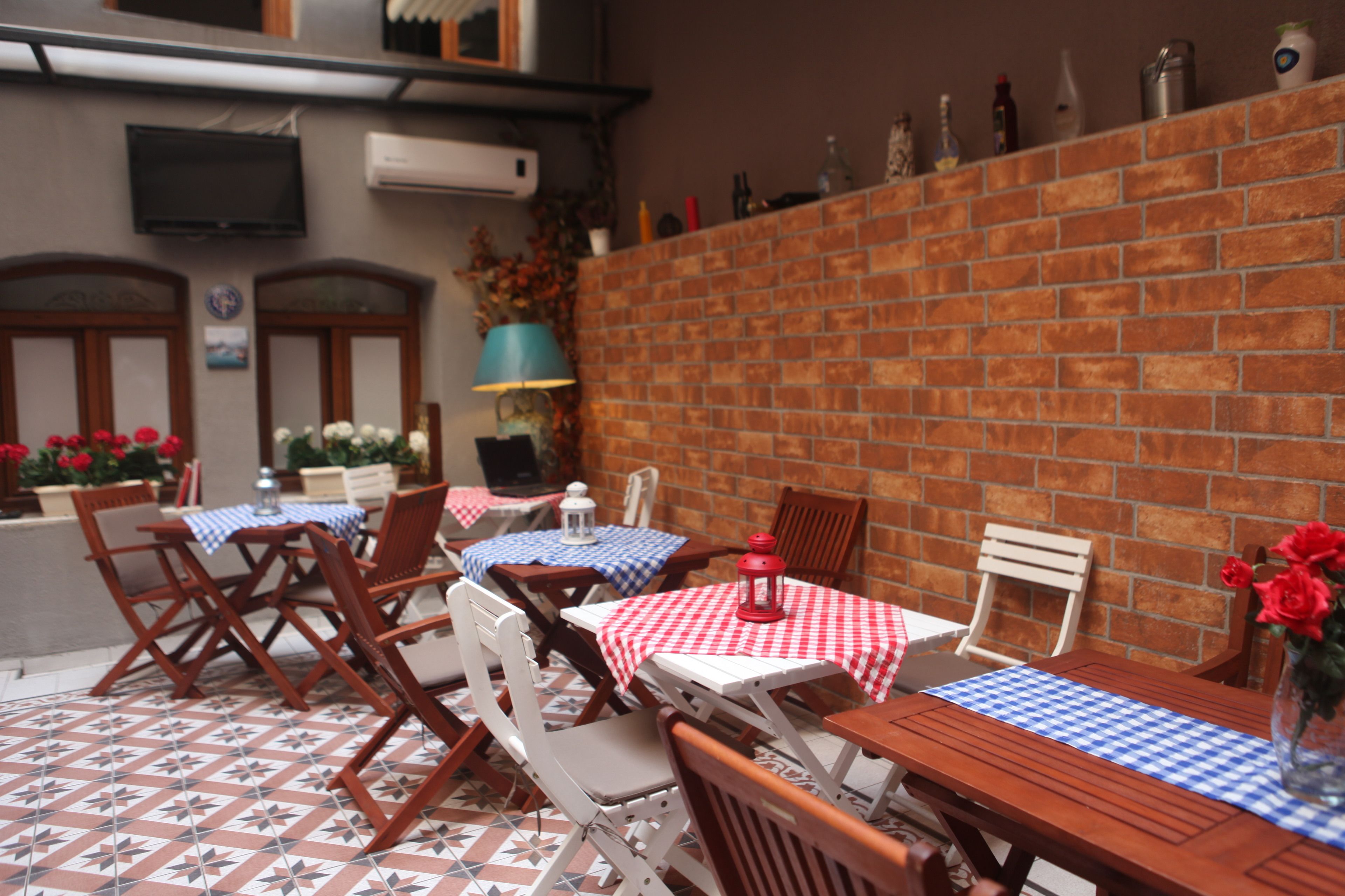 Une terrasse extérieure avec des tables et des chaises, un mur en briques et un téléviseur fixé au mur.