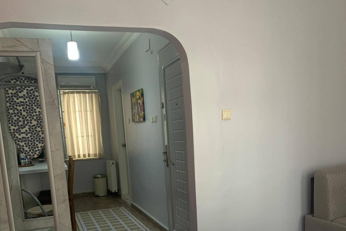 Une chambre d’hôtel comprenant un lit, une petite table, un miroir, une porte donnant sur une salle de bain et un couloir avec une fenêtre.