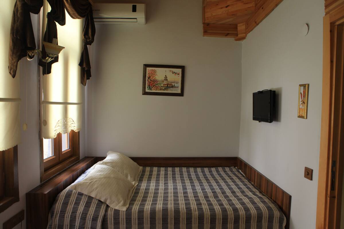 Une chambre à coucher avec un lit, une fenêtre avec des rideaux, un tableau au mur et un téléviseur.