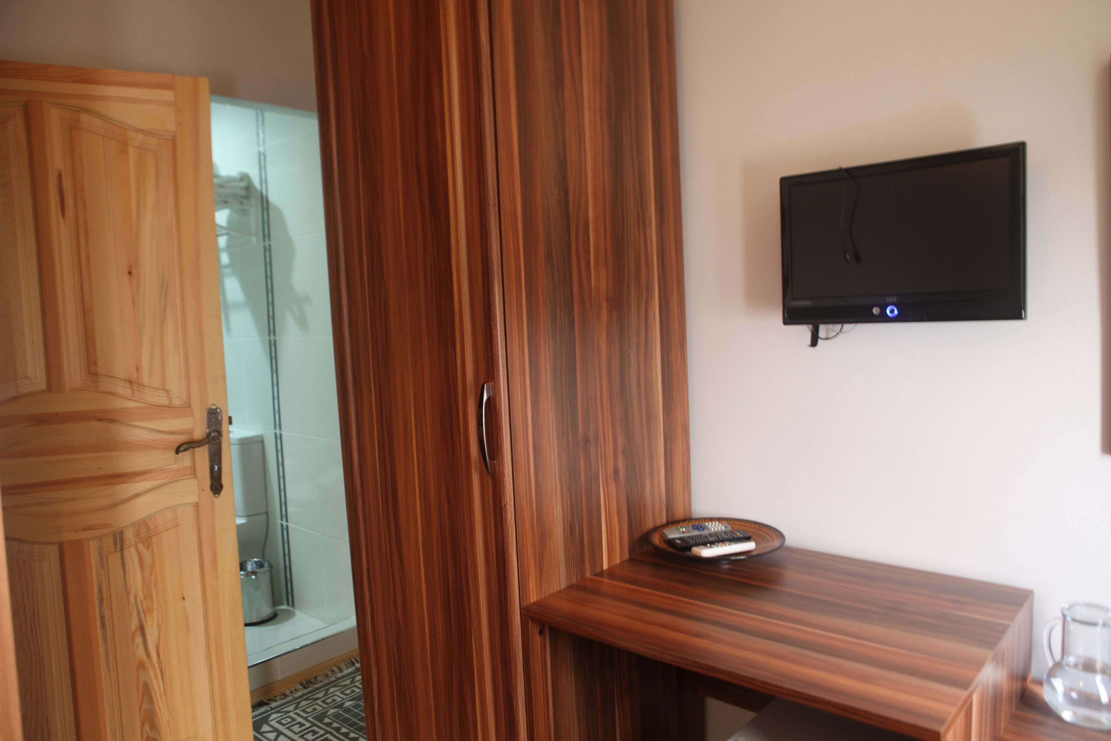 A wooden wardrobe, a bathroom with a glass shower, and a flat-screen TV on the wall.