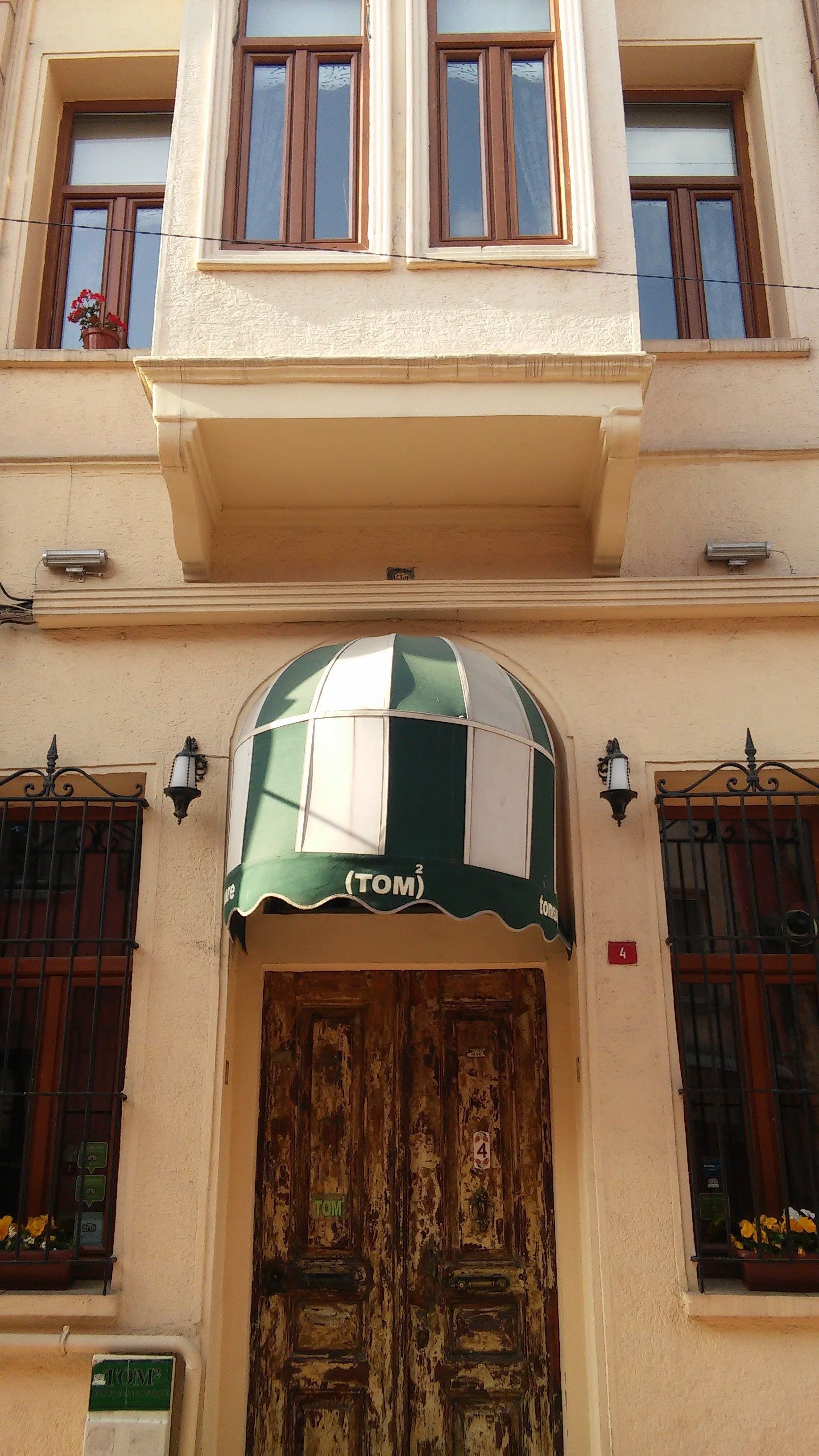 La façade d’un immeuble est ornée d’un auvent vert sur lequel on peut lire le mot « TOM », au-dessus d’une porte en bois.