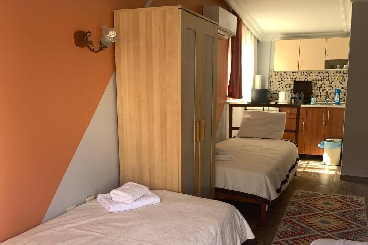 Une chambre d’hôtel avec deux lits, une armoire, un petit coin cuisine et un tapis à motifs.