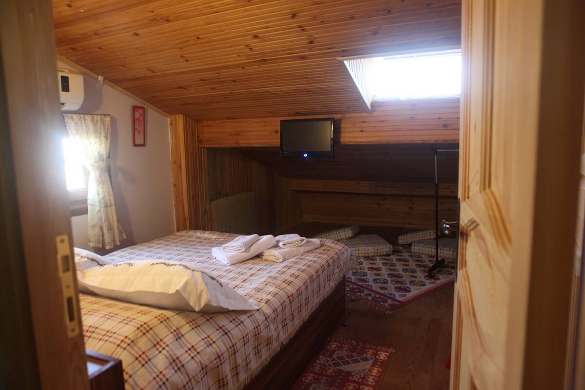 Une chambre confortable avec un lit, un téléviseur à écran plat fixé au plafond et une fenêtre avec des rideaux.
