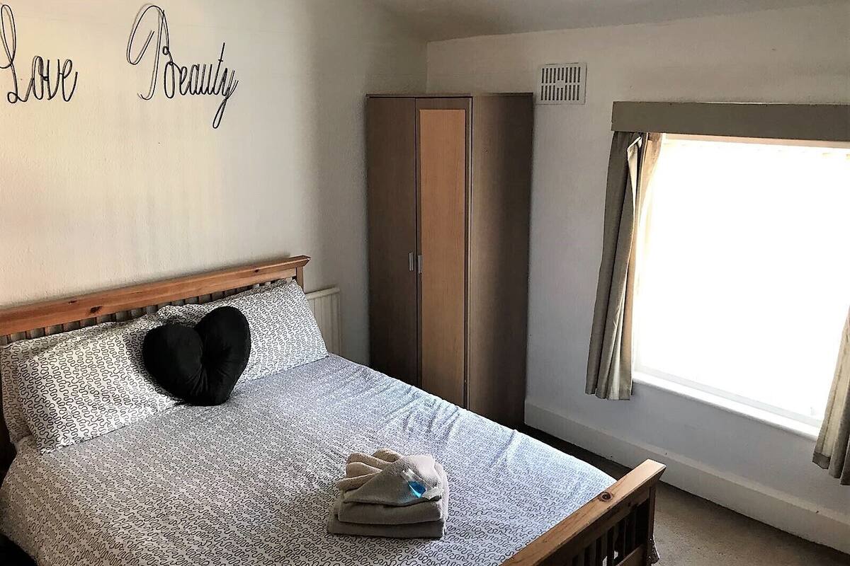 A bedroom with a bed, a wardrobe, a window with curtains, and a wall with the words "Love Beauty".