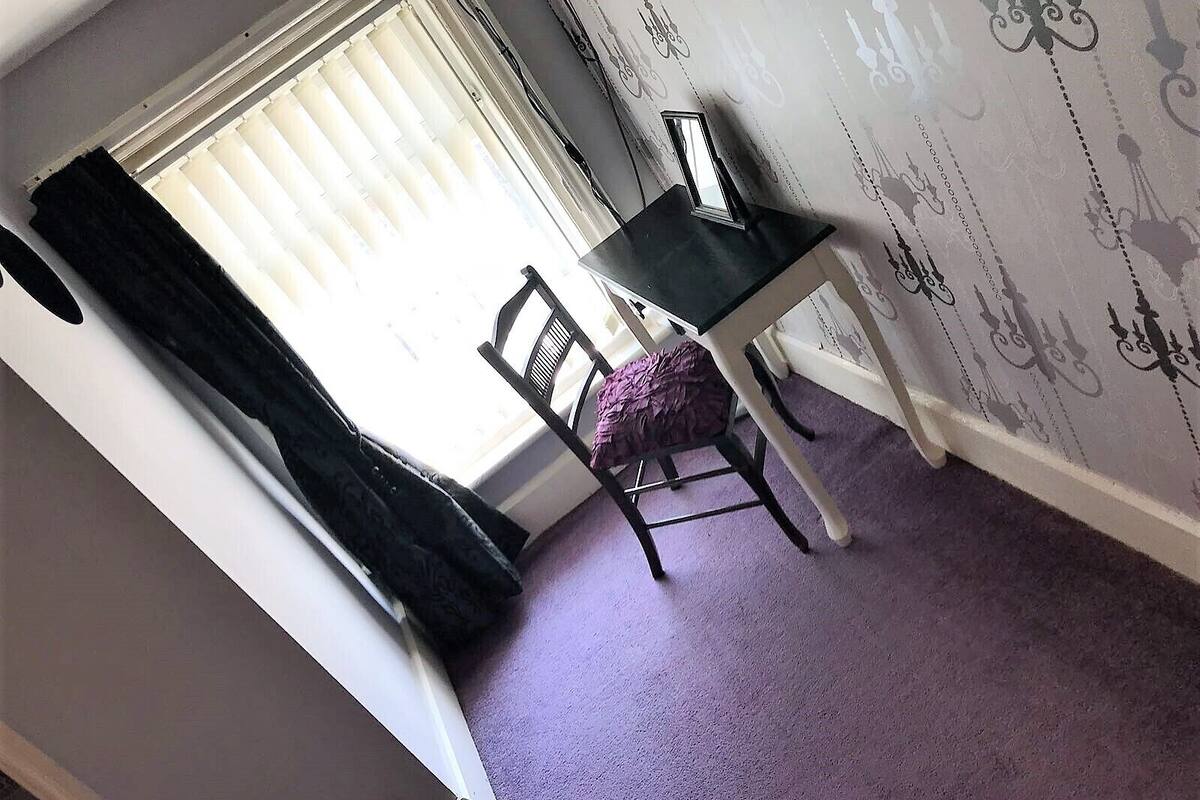 A room with a window, a chair, a small table, and a patterned wall.