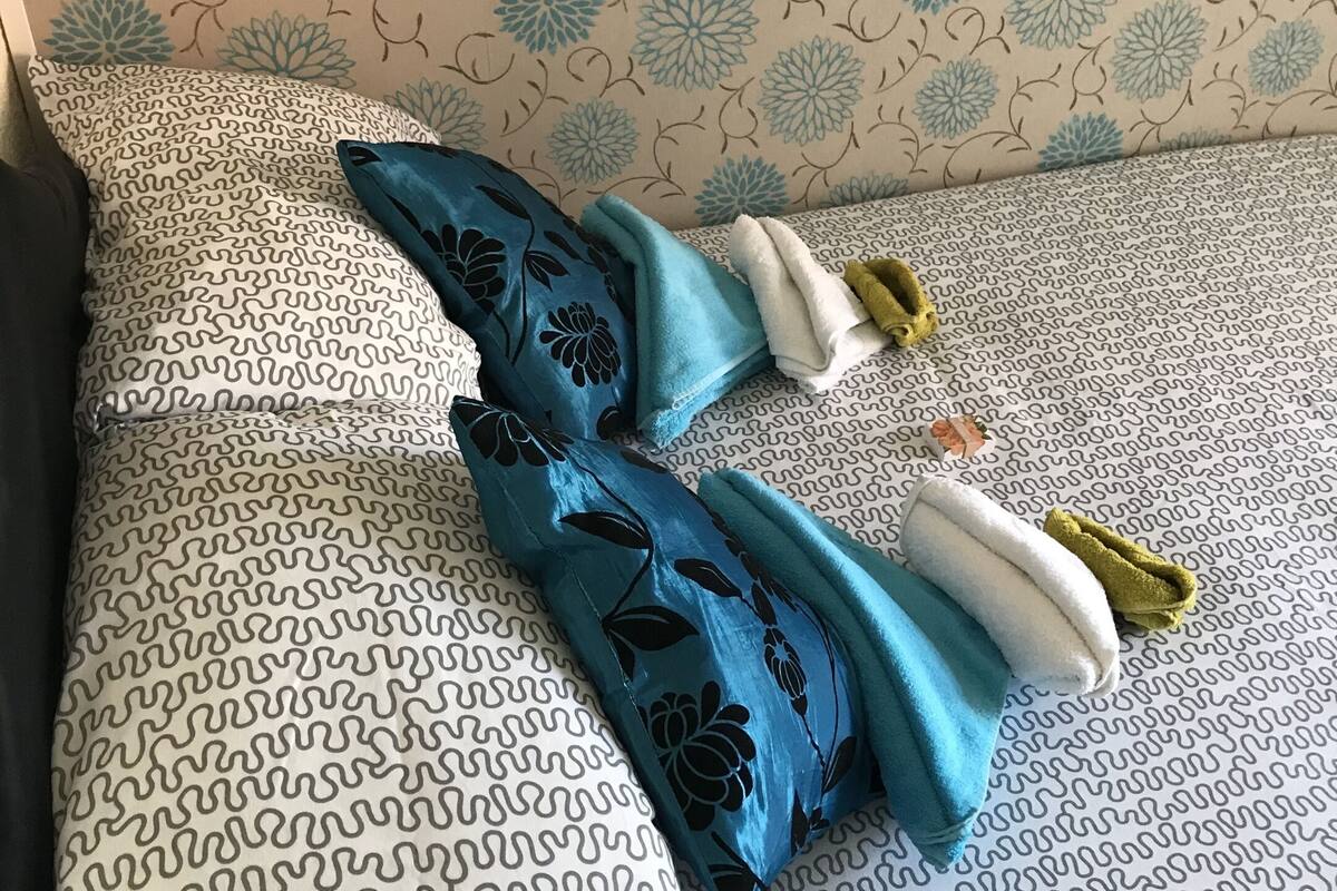 A bed with patterned bedding and pillows, a wall with floral wallpaper, and a bedside table with a lamp.