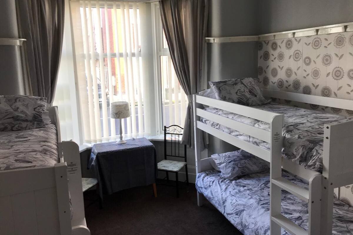 A dormitory room with bunk beds, a small table, and a chair.
