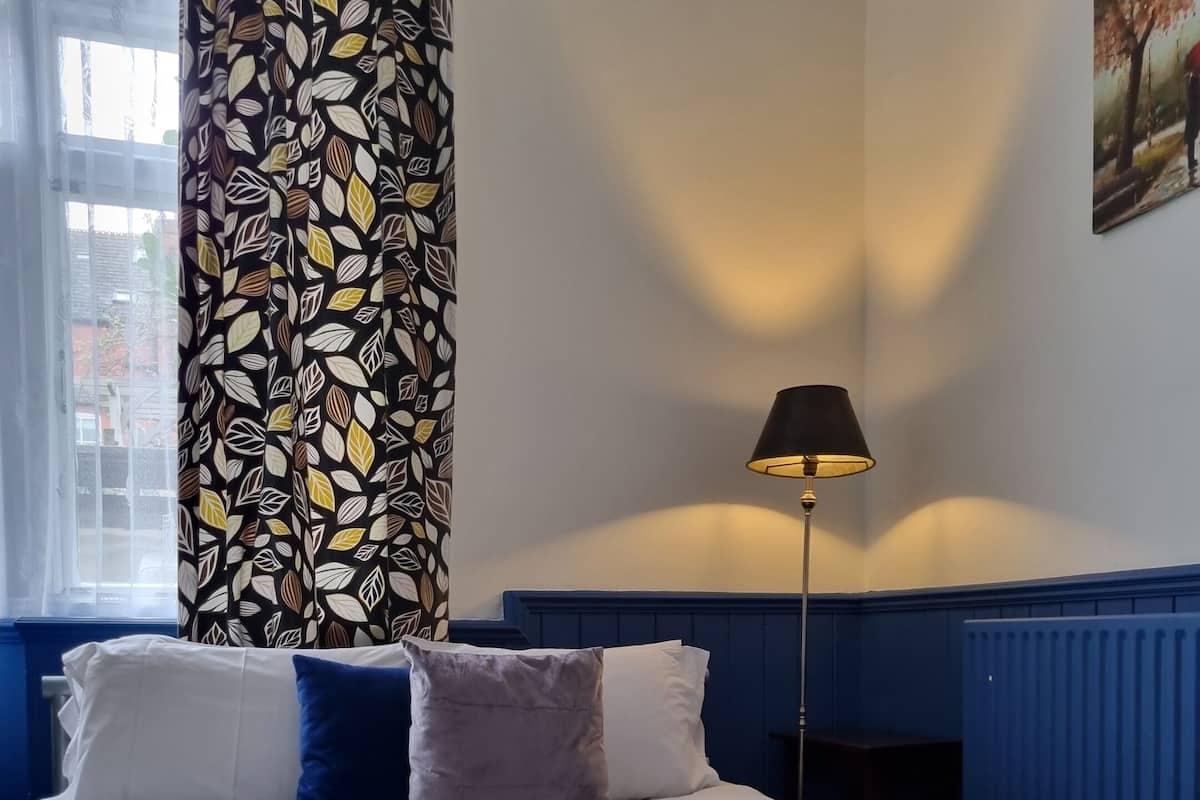 A neatly made bed with white and blue bedding, a green throw blanket, and a remote control on the pillows.