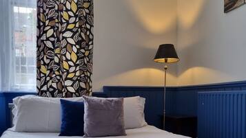 A neatly made bed with white and blue bedding, a green throw blanket, and a remote control on the pillows.