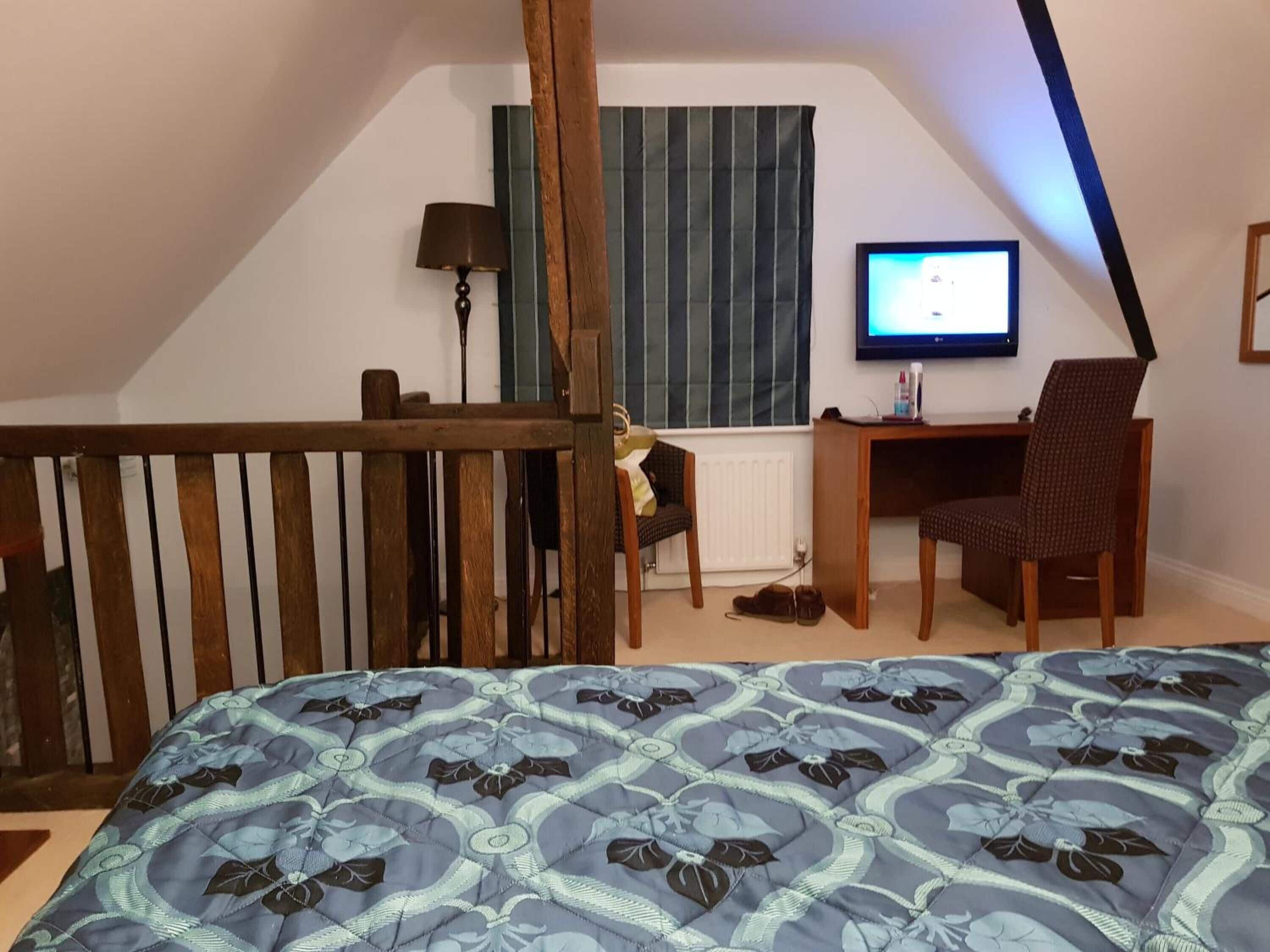 A bedroom with a bed, a desk, a chair, a television, and a window with curtains.